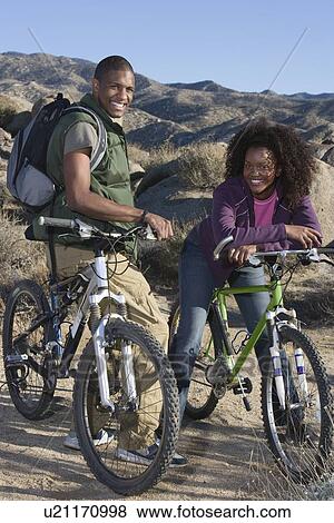 Young couple stand smiling with mountain bikes View Large Photo Image Stock Photo - Young couple stand smiling with mountain bikes. Fotosearch