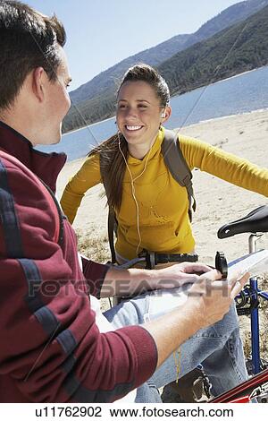 Young couple standing with mountain bikes, woman listening to earphones, man using map and compass, by lake View Large Photo Image Stock Image - Young couple standing with mountain bikes, woman listening to earphones, man using map and compass, by lake. Fotosearch