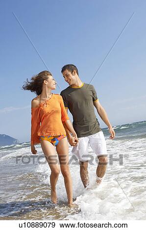 Young couple walking through surf on beach, front view View Large Photo Image Stock Photo - Young couple walking through surf on beach, front view. Fotosearch