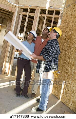 Stock Photograph - Young couple with construction worker in construction site. Fotosearch