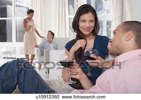 Stock Image - Young couples drinking wine in living room. Fotosearch