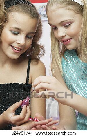 Stock Image - Young girl applying nail polish to friends fingernails. Fotosearch