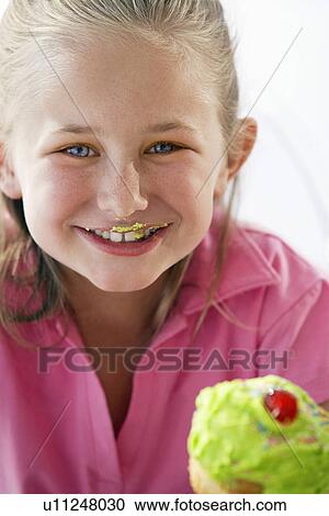 Stock Image - Young girl eating cupcake, head and shoulders. Fotosearch