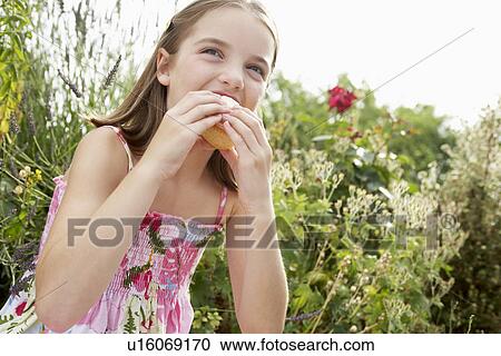 Young girl sitting in meadow eating cupcake, close up View Large Photo Image Stock Image - Young girl sitting in meadow eating cupcake, close up. Fotosearch