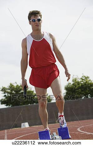 Young man by starting blocks holding relay baton View Large Photo Image Stock Image - Young man by starting blocks holding relay baton. Fotosearch