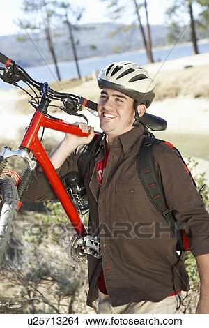 Picture - Young Man Carrying Mountain Bike in field. Fotosearch