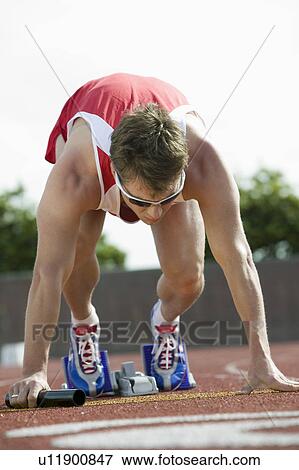 Stock Photo - Young man in starting blocks holding relay baton. Fotosearch