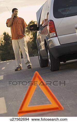 Picture - Young man looking at car behind warning triangle. Fotosearch