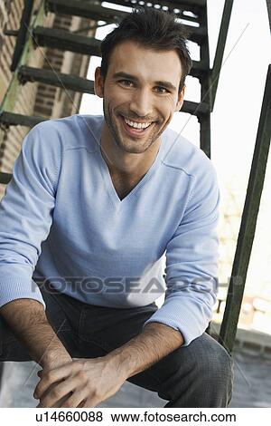 Stock Photo - Young man sitting on fire escape stairs, portrait. Fotosearch