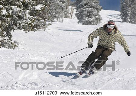 Stock Photo - Young Man Skiing down snow covered slope, full length. Fotosearch