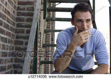 Stock Photograph - Young Man Smoking on Fire Escape. Fotosearch