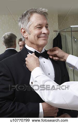 Stock Photo - Young man tying middle-aged man's bow tie. Fotosearch