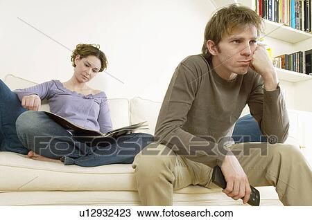 Stock Image - Young Man Watching Television with woman reading magazine behind. Fotosearch