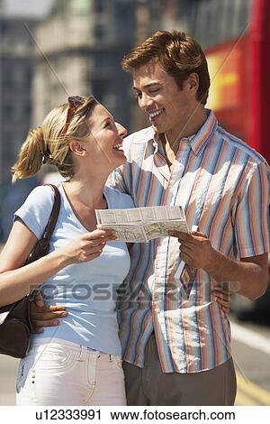 Stock Image - Young vacationing couple on London street reading map. Fotosearch