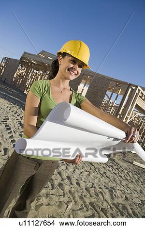 Picture - Young woman examining blueprint in construction site. Fotosearch