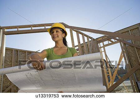 Young woman examining blueprint in construction site View Large Photo Image Stock Image - Young woman examining blueprint in construction site. Fotosearch