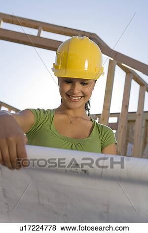 Stock Photo - Young woman examining blueprint in construction site. Fotosearch