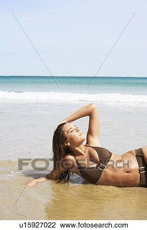 Young woman in bikini lying in surf View Large Photo Image Stock Image - Young woman in bikini lying in surf. Fotosearch