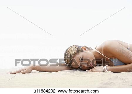 Stock Image - Young woman in bikini lying on beach, head and shoulders. Fotosearch