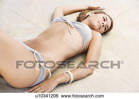 Young woman in bikini lying on beach View Large Photo Image Stock Photograph - Young woman in bikini lying on beach. Fotosearch