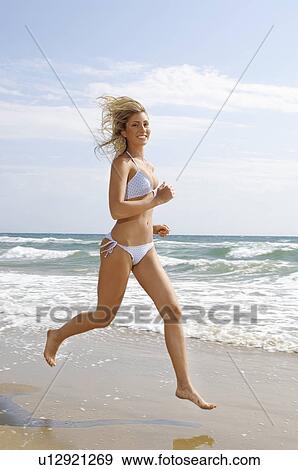 Stock Photo - Young woman in bikini running on beach, portrait, side view. Fotosearch