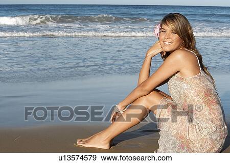 Young woman in summer dress sitting on beach, side view View Large Photo Image Stock Photo - Young woman in summer dress sitting on beach, side view. Fotosearch