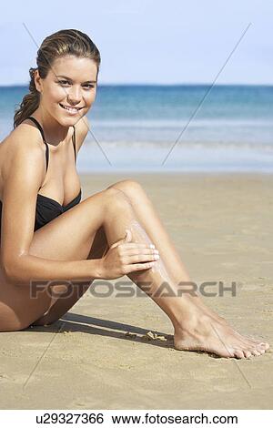 Young woman in swimsuit applying sunscreen on beach View Large Photo Image Stock Photograph - Young woman in swimsuit applying sunscreen on beach. Fotosearch