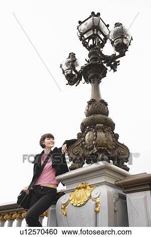 Stock Image - Young woman leaning on ornate streetlight. Fotosearch