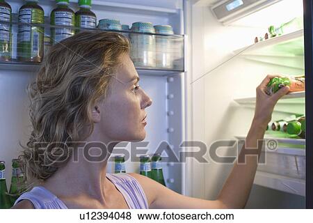 Stock Photo - Young woman looking for food in fridge. Fotosearch