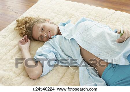 Young woman lying on bed listening to music, portrait View Large Photo Image Picture - Young woman lying on bed listening to music, portrait. Fotosearch