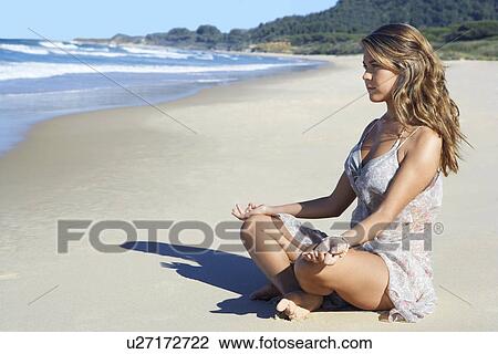 Stock Image - Young woman meditating on beach, side view. Fotosearch