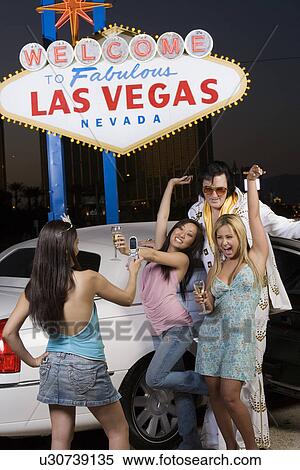 Stock Photography - Young woman photographing two friends with Elvis impersonator, "Welcome to fabulous Las Vegas" sign in background, Las Vegas, Nevada, USA. Fotosearch