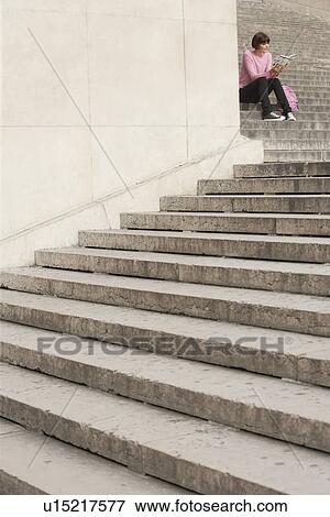 Stock Photo - Young woman reading book sitting on steps. Fotosearch