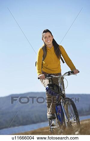 Picture - Young Woman Riding Mountain Bike by lake. Fotosearch