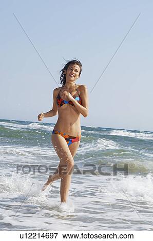Young woman running through surf on beach, front view View Large Photo Image Stock Photo - Young woman running through surf on beach, front view. Fotosearch
