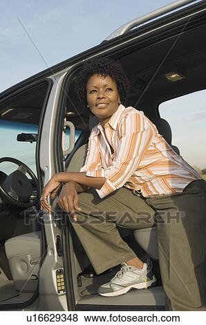 Stock Photo - Young woman sitting in open car doorway. Fotosearch