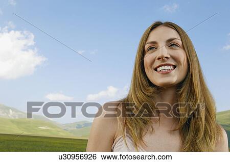 Stock Photograph - Young woman standing in mountain field, close up, front view. Fotosearch