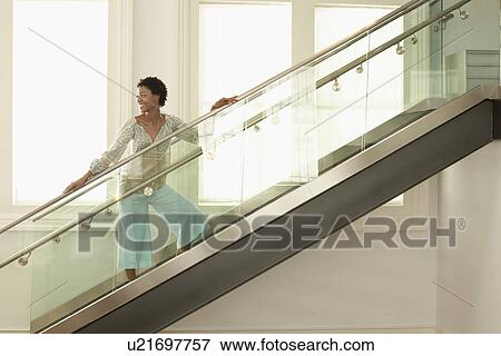 Stock Photo - Young woman standing on modern glass stairs, portrait. Fotosearch