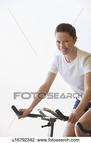 Stock Image - Young Woman Using Exercise Bike, portrait. Fotosearch