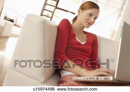 Young woman using laptop in living room View Large Photo Image Stock Photo - Young woman using laptop in living room. Fotosearch