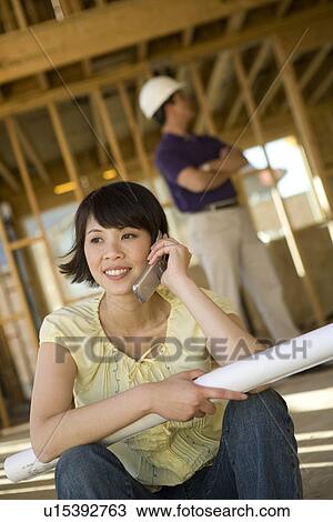 Stock Image - Young woman using mobile phone in construction site. Fotosearch