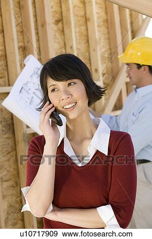 Stock Photo - Young woman using mobile phone in construction site. Fotosearch