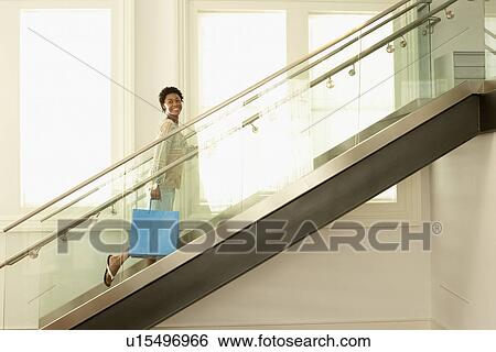Young woman walking up the modern stairs with shopping bag, portrait View Large Photo Image Stock Photograph - Young woman walking up the modern stairs with shopping bag, portrait. Fotosearch