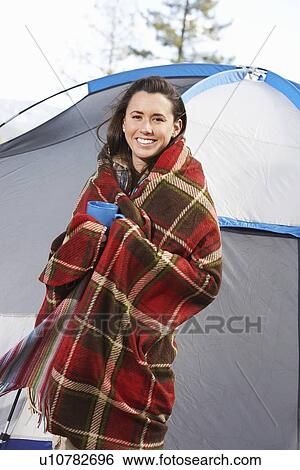 Stock Photograph - Young woman wrapped in blanket and holding mug, standing in front of tent. Fotosearch