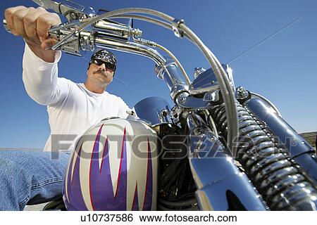 Stock Photograph - Biker riding motorcycle, low angle view. Fotosearch