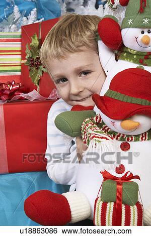 Stock Photograph - Boy (5-6) holding stuffed snowman in front of Christmas tree, portrait. Fotosearch