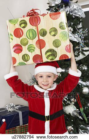 Picture - Boy (5-6) in Santa costume holding present over head. Fotosearch