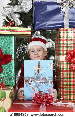 Boy (5-6) in Santa costume in pile of presents by Christmas tree View Large Photo Image Stock Photo - Boy (5-6) in Santa costume in pile of presents by Christmas tree. Fotosearch