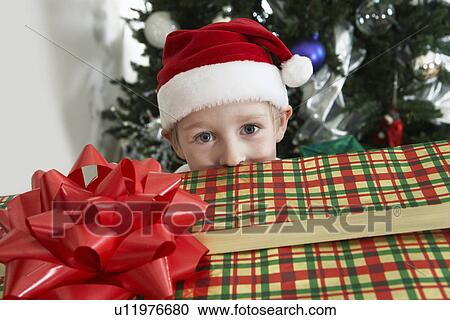 Boy (5-6) in Santa costume peeking over present by Christmas tree View Large Photo Image Stock Image - Boy (5-6) in Santa costume peeking over present by Christmas tree. Fotosearch