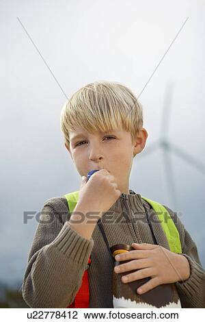 Stock Image - Boy (7-9) blowing toy whistle at wind farm, portrait. Fotosearch